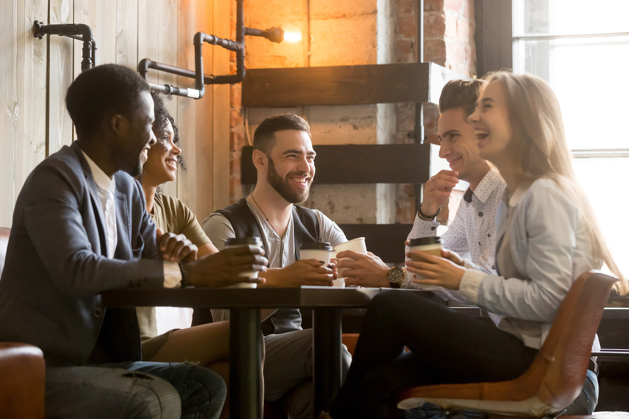 Multiracial young friends having fun laughing drinking coffee in